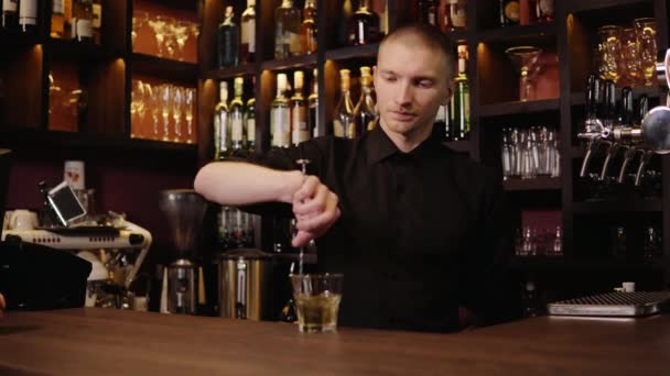 Joven barman en el interior del bar vertiendo whisky en vidrio y llevándolo para los visitantes — Vídeo de stock