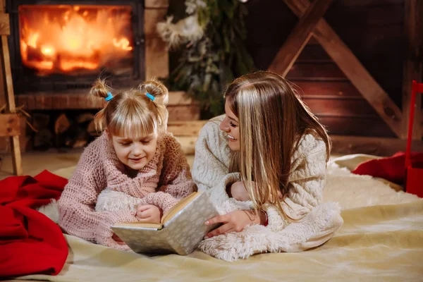 Mutlu Noeller ve mutlu yeni yıl. Güzel aile Xmas iç. Oldukça genç anne kızına Noel ağacı yakınındaki bir kitap okuma.
