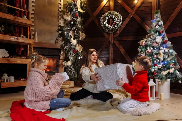 Merry Christmas and Happy New Year. Cheerful mom and her cute daughter and son exchanging gifts. Parent and children having fun near Christmas tree indoors. Loving family with presents in room. — Stock Photo, Image