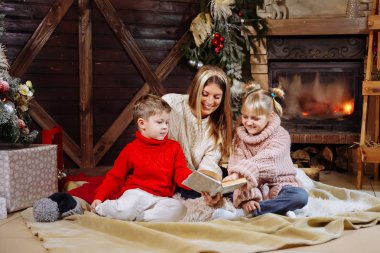 Mutlu Noeller ve mutlu yeni yıl. Güzel aile Xmas iç. Oldukça Genç Anne kızı ve oğlu yakınındaki Noel ağacı için bir kitap okuma.