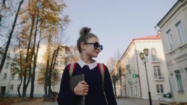 Eski Şehir caddeden aşağı yürüyüş ve gülümseyen güzel hipster genç kız. Kırmızı çanta laptop elinde tutan ile kız öğrenci. Güzel sonbahar hava.