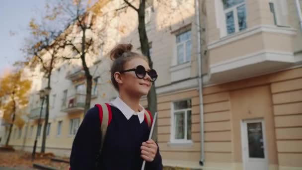 Bastante hipster adolescente chica caminando por la vieja calle de la ciudad y sonriendo. Colegiala con bolsa roja sosteniendo portátil en su mano. Hermoso clima de otoño . — Vídeos de Stock