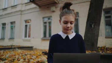 Sonbahar şehir sokak ve çalışma dizüstü bilgisayar kaldırımda oturan genç kız güzel hipster kapatın. Açık Not defteri kullanarak kız öğrenci. Güzel sonbahar hava.