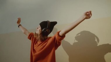 Sevimli Genç kız kulaklık ve dans, kentsel tarzı, şık hipster teen siyah şapka dinle müzik ve gülümseme sarı duvarına, turuncu çılgın sokak stil infront müzik dinleme