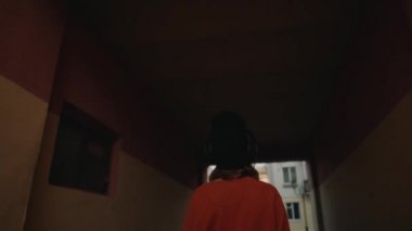 Sevimli Genç kız yürüyüş sokak arasında binalar ve kulaklık, kentsel tarzı, siyah şapkalı şık hipster teen müzik dinleme dinlemek müzik ve gülümseme, turuncu deli tarzı