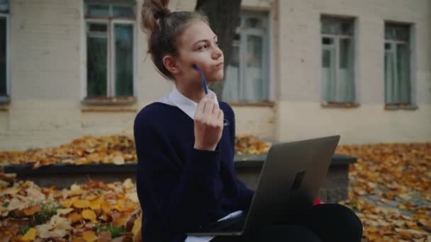 Nahaufnahme hübsches Hipster-Teenie-Mädchen, das auf einem Bürgersteig in der herbstlichen Stadtstraße sitzt und am Laptop arbeitet. Schulmädchen mit Notebook im Freien. Schönes Herbstwetter. — Stockvideo