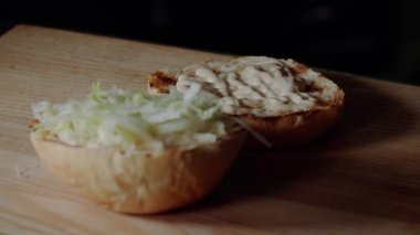 Hamburger yapma Şef. ızgara ekmek kızartma, koyarak dilimlenmiş salatalık turşusu