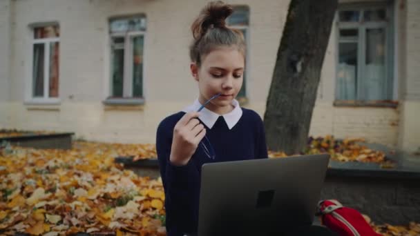 Bliska pretty hipster teen dziewczyna siedzi na chodniku na ulicy miasta jesień i pracującym laptopem. Uczennica, które przy użyciu notebooka odkryty. Piękna jesienna pogoda. — Wideo stockowe