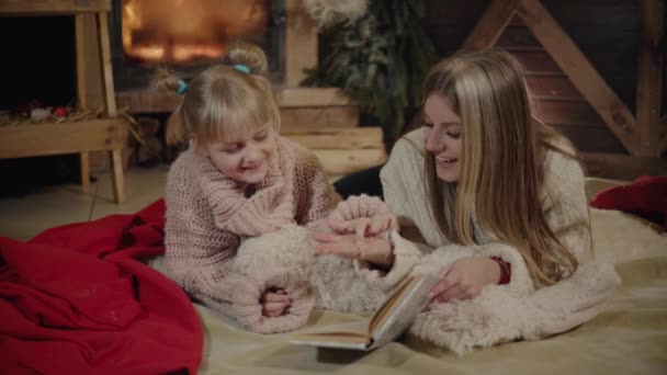 기쁜 성 탄과 새 해 복 많이 받으세요입니다. 크리스마스 인테리어에 아름 다운 가족입니다. 크리스마스 트리 근처 그녀의 딸에 게 책을 읽고 꽤 젊은 어머니. — 비디오