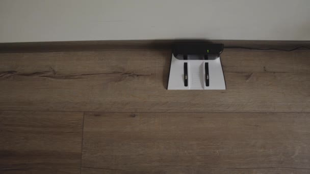 En robot dammsugare glider över ett modernt vardagsrum och drar in i laddningen. 4K. uppifrån. — Stockvideo