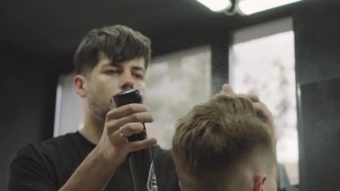 Çekici erkek berber dükkanında modern bir saç kesimi oluyor. Berber sprey ile saç ıslak ve onları tarak. El yapımı atış. 4k.