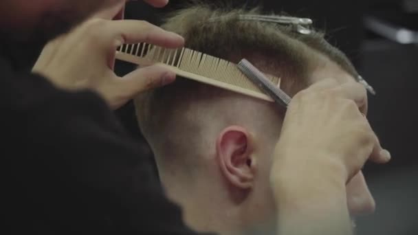 Holič stříhá nůžkami klientovi vlasy. Zavřít. Atraktivní samec se nechá ostříhat v holičství. Ruční střelba. 4K. — Stock video