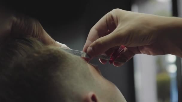 Barbier professionnel avec rasoir à gorge tranchante ouvert rase les cheveux sur les tempes mans. Attrayant mâle obtient une coupe de cheveux moderne dans le salon de coiffure. Ferme là. Tir à la main. 4K .