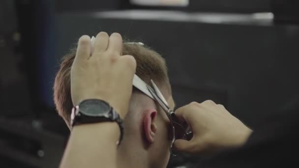 Peluquero corta el cabello del cliente con tijeras. De cerca. Hombre atractivo está consiguiendo un corte de pelo moderno en la peluquería. Un disparo de mano. 4K . — Vídeo de stock