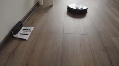 Robotik elektrikli süpürge modern bir oturma odası boyunca kayar ve şarj içine çeker. 4k.