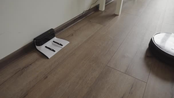 Un aspirateur robotisé glisse à travers un salon moderne et se tire dans la charge. 4K . — Video