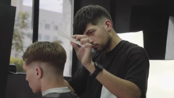 Peluquero corta el cabello del cliente con tijeras. De cerca. Hombre atractivo está consiguiendo un corte de pelo moderno en la peluquería. Un disparo de mano. 4K . — Vídeo de stock