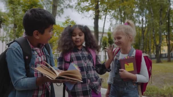 Zpátky do školy. Zavři tři přátele s batohy a smát se před školou. Smíšená rasová skupina škola děti se baví na školním dvoře. Výstřel z pomalého pohybu. — Stock video