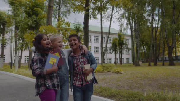 Terug naar school. Drie vrienden met rugzakken huging en lachen voor de school. Gemengde rassengroep school kinderen plezier in de Schoolyard. Slow Motion-opname. — Stockvideo