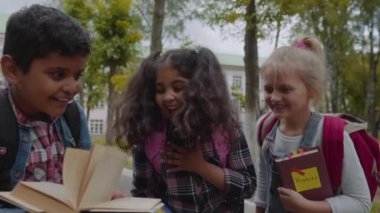 Okula geri dön. Sırt çantaları ile yakın Üç Arkadaş sarılma ve okul önünde gülüyor. Okul bahçesinde eğlenen Okul Çocukları Karışık Irk Grubu. Yavaş Çekim Çekimi.