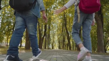 Sırt Çantalı İki Arkadaş Okula Gidiyor. Parkta Yürüyen Okul Çocuklarının Karışık Irk Grubu'nun Arka Görünümü. Yavaş Çekim Çekimi.