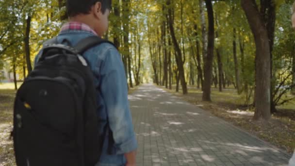 Två vänner med ryggsäckar går till skolan. Tillbaka syn på blandade ras grupp av skol barn som går i parken. Slow motion shot. — Stockvideo