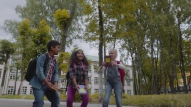 Okula dönüyoruz. Üç arkadaş backpacks Ile sarılmaya ve okulun önünde gülüyor. Karışık ırksal grup okul çocuklar okulda kitap atma eğlenceli sahip. Yavaş hareket çekimi.