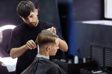 Berber müşterinin saçını makasla keser. Yakından kapatın. Çekici erkek berber dükkanında modern bir saç kesimi oluyor.