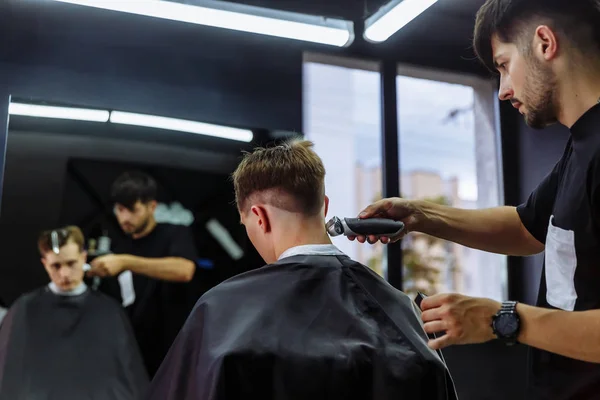 Male haircut with electric razor. Barber makes haircut for client at the barber shop by using hairclipper. Man hairdressing with electric shaver.