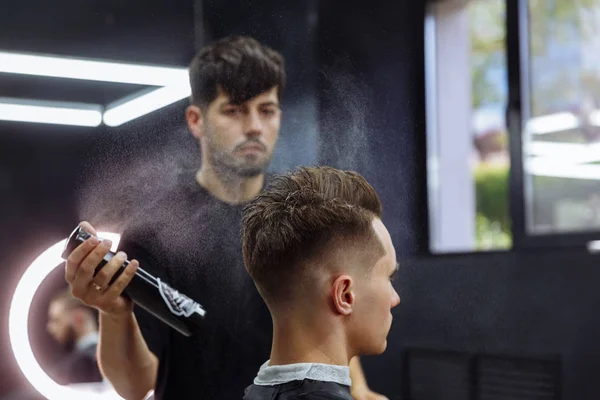 Барбер робить зачіску з розпилювачем волосся після стрижки в перукарні. Молодий гарний кавказький чоловік стрижеться у сучасному перукарні.. — стокове фото