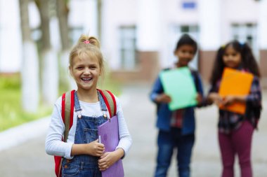 Okula dönüyoruz. Backpacks Ile üç arkadaş yakın yukarı sarılmaya ve okulun önünde gülüyor. Okul çocuklar karışık ırk grup okulda eğlenmek.