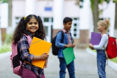 Okula dönüyoruz. Backpacks Ile üç arkadaş yakın yukarı sarılmaya ve okulun önünde gülüyor. Okul çocuklar karışık ırk grup okulda eğlenmek.