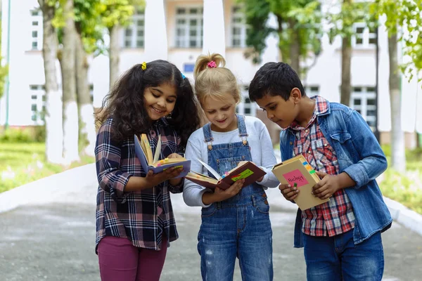 Torniamo a scuola. Chiudi Tre amici con gli zaini che si abbracciano e ridono davanti alla scuola. Gruppo misto razziale di bambini della scuola che si divertono nel cortile della scuola . — Foto Stock