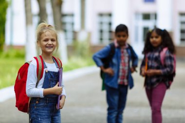 Okula dönüyoruz. Backpacks Ile üç arkadaş yakın yukarı sarılmaya ve okulun önünde gülüyor. Okul çocuklar karışık ırk grup okulda eğlenmek.