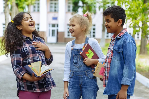 Okula dönüyoruz. Backpacks Ile üç arkadaş yakın yukarı sarılmaya ve okulun önünde gülüyor. Okul çocuklar karışık ırk grup okulda eğlenmek. — Stok fotoğraf