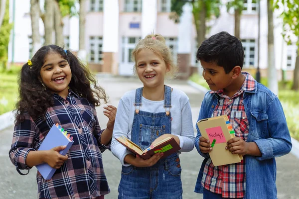 Torniamo a scuola. Chiudi Tre amici con gli zaini che si abbracciano e ridono davanti alla scuola. Gruppo misto razziale di bambini della scuola che si divertono nel cortile della scuola . — Foto Stock