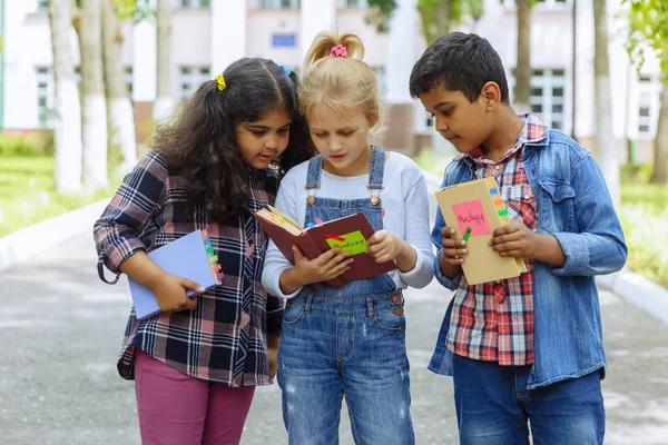 Okula dönüyoruz. Backpacks Ile üç arkadaş yakın yukarı sarılmaya ve okulun önünde gülüyor. Okul çocuklar karışık ırk grup okulda eğlenmek.