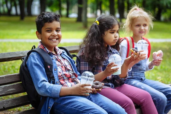 Vegyes faji csoport iskolás gyerekek ebédet eszik együtt a break szabadban közelében iskolába. Vissza az iskolai koncepcióhoz. — Stock Fotó