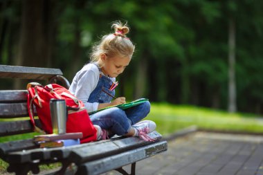 Renkli kalemler ile çizim küçük güzel okul kız, güneşli parkta bir bankta oturan