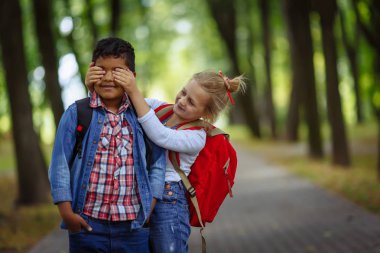 İki okul arkadaşları parkta eğleniyor. Kafkas kız gözlerini kapsayan Afro Amerikan çocuk şaşırttı.