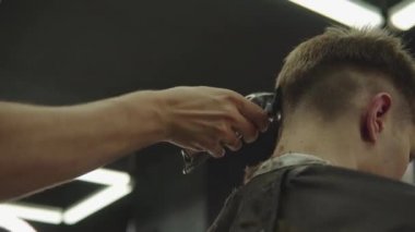 Elektrikli traşlı erkek saç kesimi. Saç kesme stilini kapat. Berber, berber dükkanında saç kesme makinesi kullanarak müşterisinin saçını kesiyor. Elektrikli traşlı erkek kuaförü. El kamerasıyla. 4K.