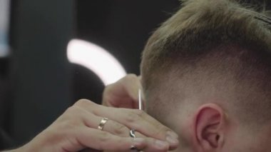 Berber, müşterinin saçını makasla keser. Kapatın. Çekici erkek berber dükkanında modern bir saç kesimi yaptırıyor. El kamerasıyla. 4K.