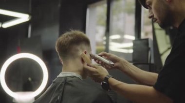 Elektrikli jiletle erkek saç kesimi. Berber kuaför kullanarak berber dükkanında müşteri için saç kesimi yapar. Elektrikli tıraş makinesi ile erkek kuaförlük. El yapımı atış. 4k.