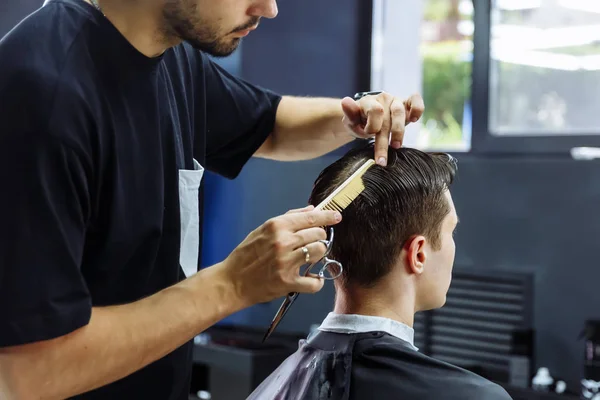 Barbeiro corta o cabelo do cliente com uma tesoura. Fecha. Homem atraente está recebendo um corte de cabelo moderno na barbearia . — Fotografia de Stock