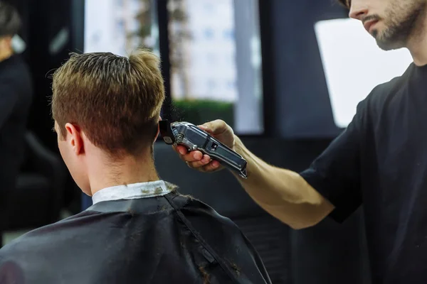 Male haircut with electric razor. Barber makes haircut for client at the barber shop by using hairclipper. Man hairdressing with electric shaver.