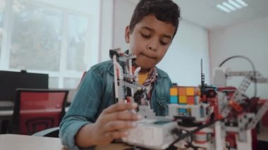 Robot iktisat okulundaki küçük çocuk robot yapıyor. Afro-Amerikalı genç öğrenci fütüristik bir robotmodel kiti montaj. 4k.