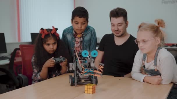 Blandad ras grupp av skolbarn kontrollera robot maskin med fjärrkontroll tillsammans lärare. Kreativa barn som arbetar med det tekniska projektet i skolan. — Stockvideo