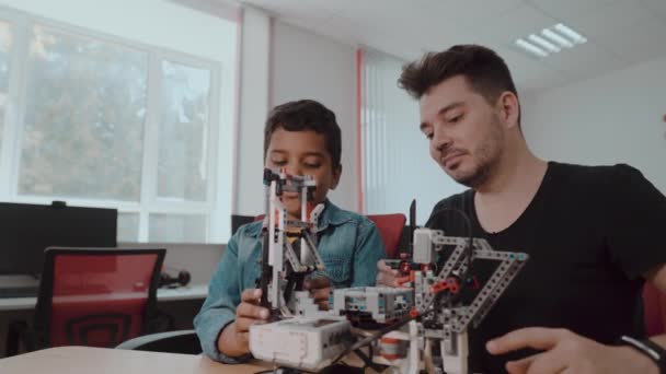 Eine gemischte Gruppe von Schulkindern steuert gemeinsam mit einem Lehrer Roboter mit Fernbedienung. Kreative Kinder arbeiten in der Schule am Tech-Projekt. — Stockvideo
