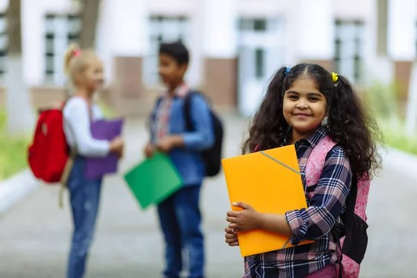 Okula dönüyoruz. Backpacks Ile üç arkadaş yakın yukarı sarılmaya ve okulun önünde gülüyor. Okul çocuklar karışık ırk grup okulda eğlenmek.