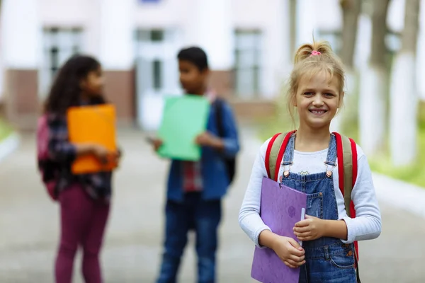 Okula dönüyoruz. Backpacks Ile üç arkadaş yakın yukarı sarılmaya ve okulun önünde gülüyor. Okul çocuklar karışık ırk grup okulda eğlenmek. — Stok fotoğraf